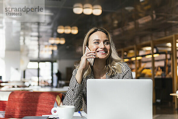 Lächelnde weibliche Fachkraft  die mit einem Mobiltelefon spricht  während sie im Café wegschaut
