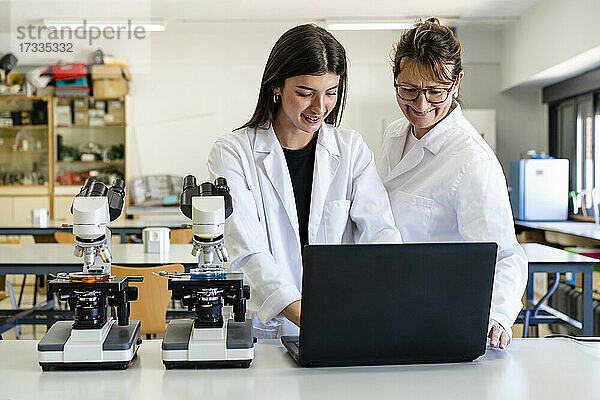 Lächelnde Wissenschaftlerinnen bei der Arbeit am Laptop im Labor