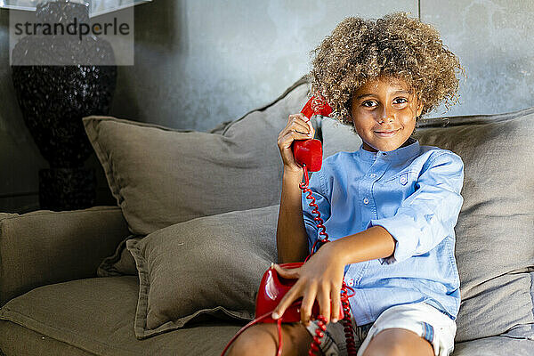 Junge mit Spielzeugtelefon  der zu Hause auf dem Sofa sitzt