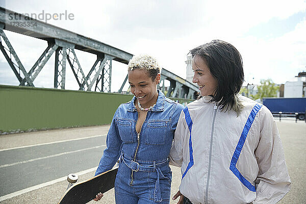 Lächelnde Frau sieht ihre Freundin an  während sie auf einer Brücke spazieren geht