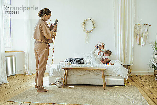 Frau fotografiert Mann beim Spielen mit Tochter auf dem Bett zu Hause