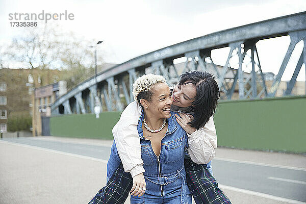 Lächelnde Frau  die ihre Freundin auf einer Brücke huckepack nimmt