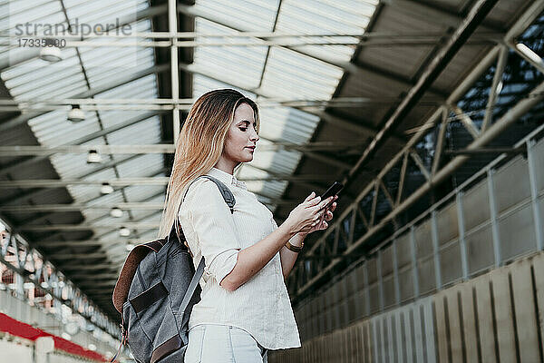 Junge Frau mit Rucksack und Smartphone am Bahnhof