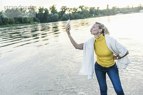 Frau knutscht  während sie ein Selfie mit ihrem Smartphone am Flussufer macht