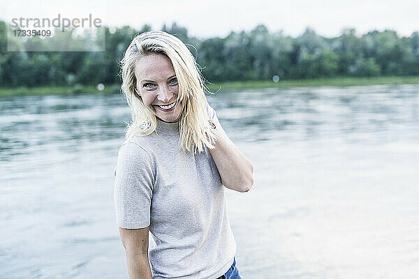 Blonde Frau lächelt  während sie am Fluss steht