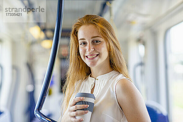 Schöne Geschäftsfrau lächelt  während sie eine Einweg-Kaffeetasse im Zug hält