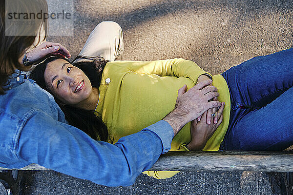 Lächelnde Frau sieht ihren Mann an  während sie auf dem Schoß im Park liegt