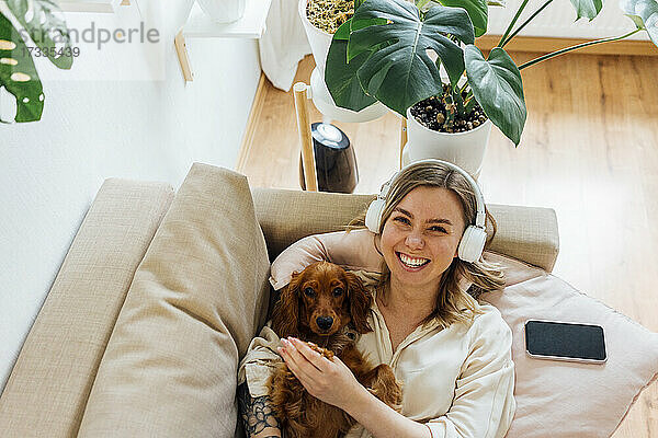Glückliche Frau mit Cocker Spaniel entspannt auf Sofa im Wohnzimmer