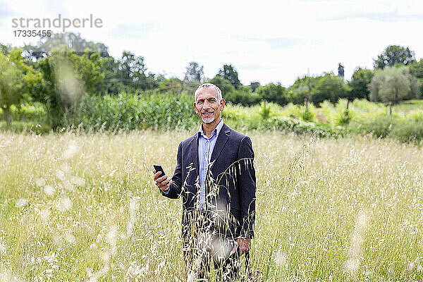 Geschäftsmann hält sein Smartphone in der Hand  während er in einem Feld steht