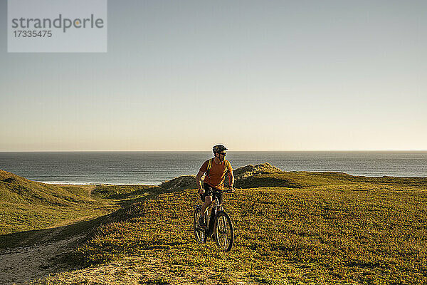 Männlicher Sportler auf dem Fahrrad in grüner Landschaft bei Sonnenuntergang