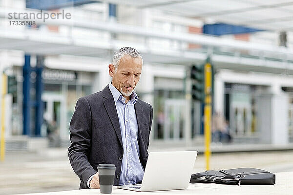 Geschäftsmann arbeitet am Laptop auf dem Bahnhof