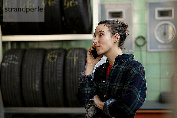 Weiblicher Mechaniker schaut weg  während er am Reifenständer in der Werkstatt mit seinem Handy spricht