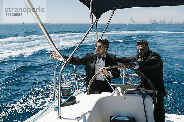 Lächelnder Mann  der auf einer Yacht auf einen männlichen Freund zeigt  an einem sonnigen Tag
