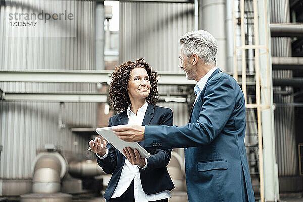 Geschäftsfrau  die ein digitales Tablet benutzt  während sie sich mit einem Kollegen vor einem Industriegebäude unterhält