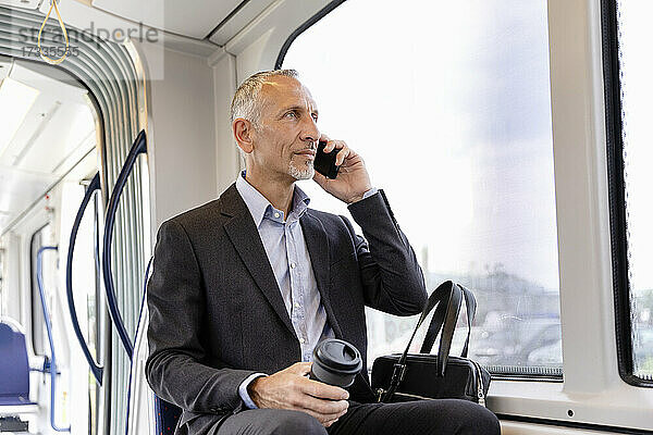 Geschäftsmann  der in der Straßenbahn sitzt und mit seinem Smartphone telefoniert