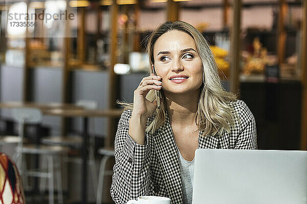 Schöne weibliche Fachkraft  die in einem Café sitzt und mit einem Smartphone spricht