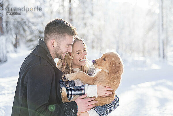 Fröhlicher Mann und Frau mit Hund im Winter