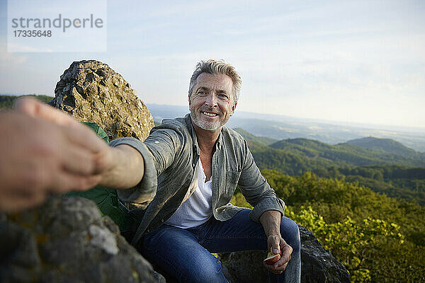 Lächelnder Mann gibt einer Freundin einen Apfel  während er auf einem Berg sitzt