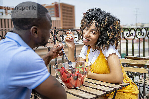 Mann und Frau essen Obstsalat  während sie auf dem Balkon sitzen