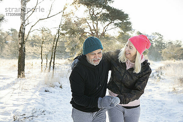 Fröhliches älteres Paar  das sich beim Spaziergang im Schnee an den Händen hält