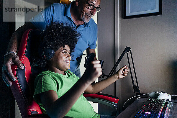 Fröhlicher Junge  der mit seinem Großvater den Sieg feiert  während er zu Hause ein Videospiel spielt