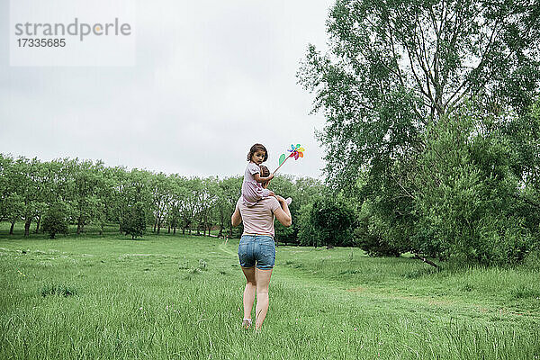 Mutter trägt Tochter auf den Schultern beim Spaziergang im Park
