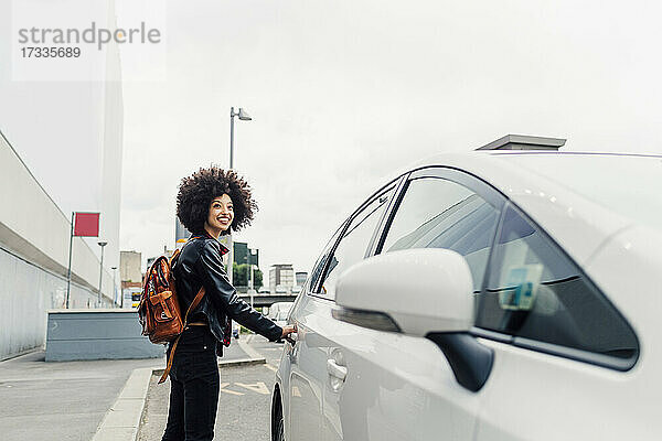 Lächelnde Frau mit Rucksack öffnet Taxitür