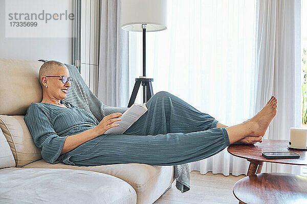 Frau liest ein Buch und entspannt sich auf dem Sofa zu Hause