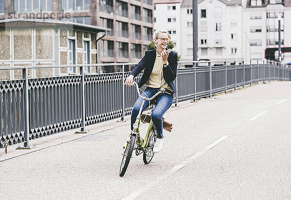 Glückliche Pendlerin  die mit ihrem Handy spricht  während sie auf einer Brücke Fahrrad fährt