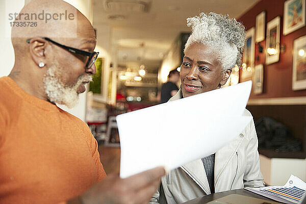 Ältere weibliche Kollegin betrachtet einen Geschäftsmann  der ein Dokument im Restaurant hält