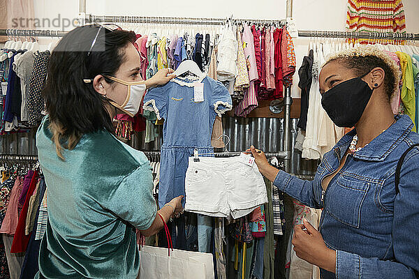 Freundinnen zeigen sich gegenseitig Kinderkleidung im Geschäft während der Pandemie