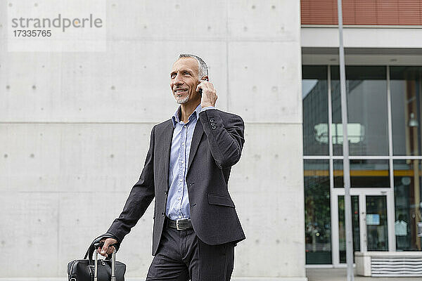 Geschäftsmann  der mit seinem Smartphone telefoniert  während er vor einem Bürogebäude steht