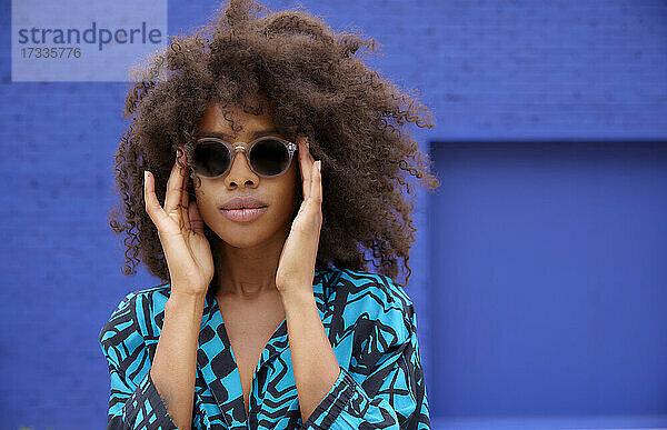 Afro-Frau mit Sonnenbrille vor einer blauen Wand