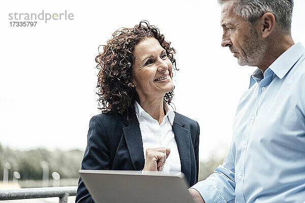Lächelnde Geschäftsfrau mit Blick auf einen Kollegen  der ein digitales Tablet hält