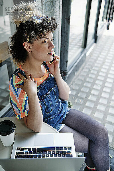 Junge Frau  die in einem Straßencafé sitzt und mit ihrem Smartphone telefoniert
