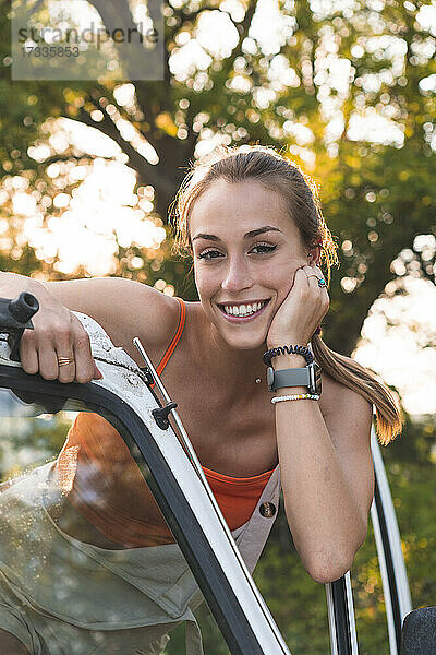 Lächelnde junge Frau lehnt an der Autotür