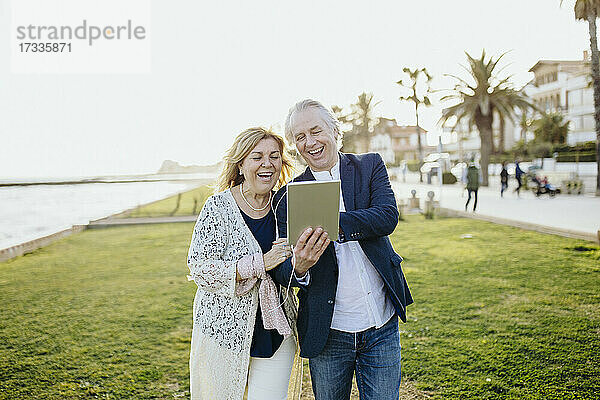 Glückliches reifes Paar teilt sich ein digitales Tablet  während es im Urlaub ein Video ansieht
