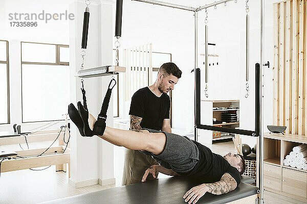 Männlicher Ausbilder  der einem Mann im Studio Pilates-Übungen beibringt