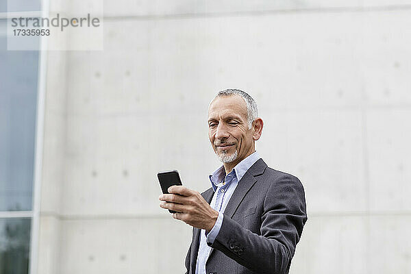 Männlicher Geschäftsmann  der in der Nähe eines Bürogebäudes ein Smartphone benutzt