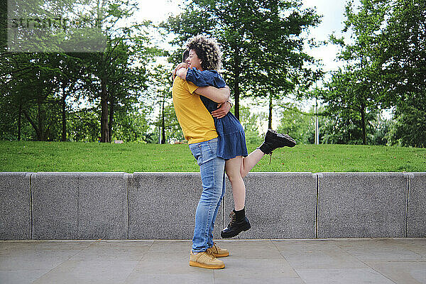 Junger Mann hebt Freundin beim Umarmen im Park hoch