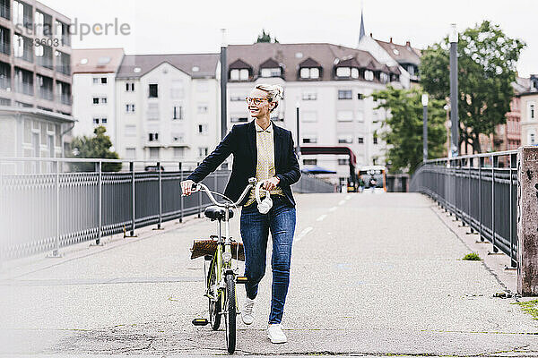 Ältere Geschäftsfrau mit Fahrrad auf einer Brücke in der Stadt