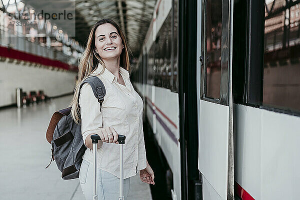 Glückliche  schöne  junge Passagierin steht mit Gepäck im Zug am Bahnhof
