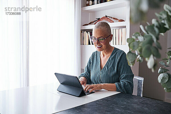 Lächelnde Frau mit rasiertem Kopf  die zu Hause ein digitales Tablet benutzt