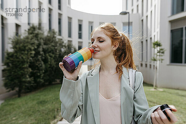 Geschäftsfrau trinkt Wasser aus einer Regenbogenflasche im Büropark