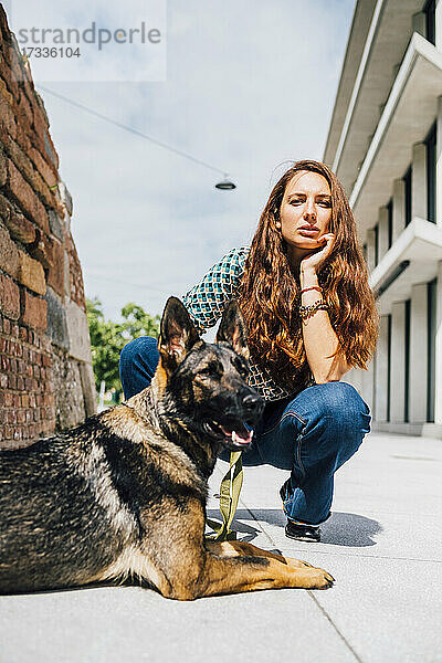 Frau kauert bei einem Hund auf dem Fußweg an einem sonnigen Tag