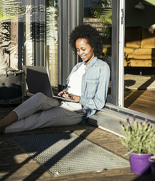 Junge Frau  die einen Laptop benutzt  während sie auf dem Balkon sitzt
