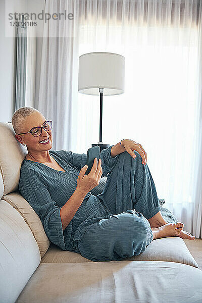 Frau hält Smartphone  während sie zu Hause auf dem Sofa sitzt