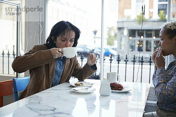 Junge Frau trinkt Kaffee und sitzt mit ihrer Freundin im Cafe