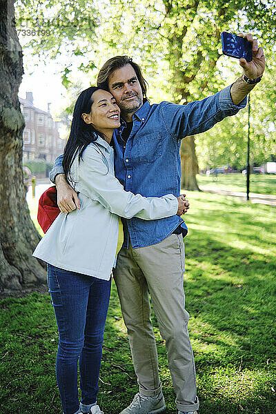 Ein schwangeres Paar macht ein Selfie mit seinem Smartphone in einem öffentlichen Park