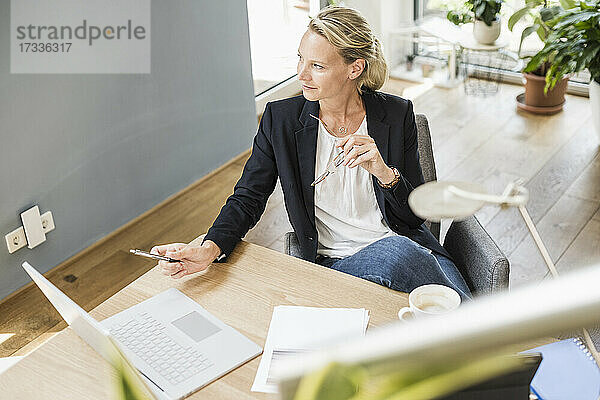 Weibliche Fachkraft hält eine Brille  während sie im Büro sitzt